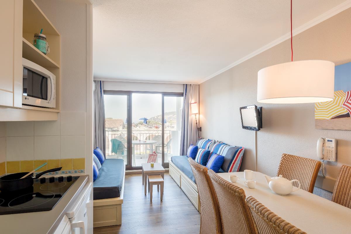Lys, moderne stue og spisestue med sofaer, spisebord, kjøkkenkrok og store vinduer ut mot en balkong med utsikt.