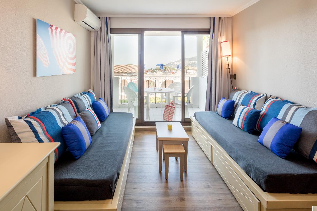 Lys stue med to sofaer, fargerike puter, et lite bord og glassdører ut til en balkong med stoler.
