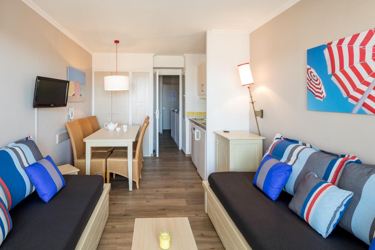 Lys, moderne stue og kjøkken med stripete sofaer, spisebord og blå og røde innredningsdetaljer.
