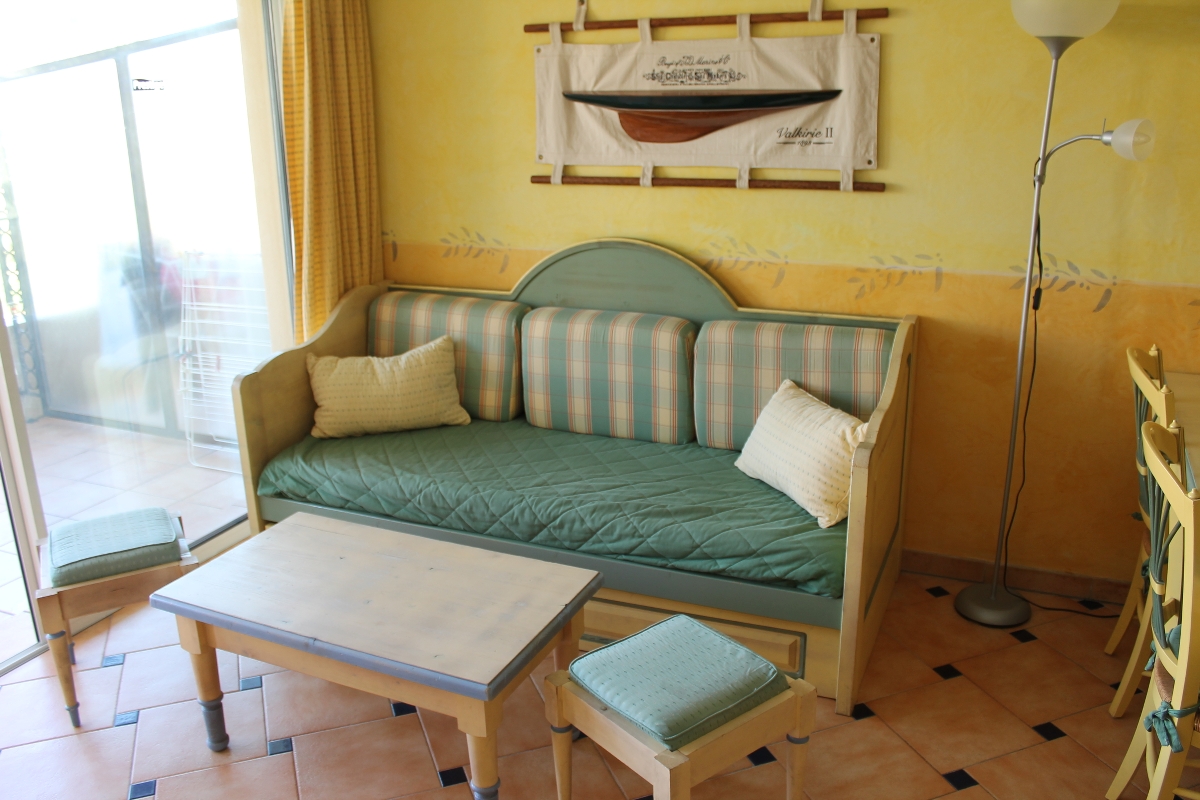 En koselig stue med sofa, puter, salongbord, to krakker og veggkunst av en båt over sofaen.