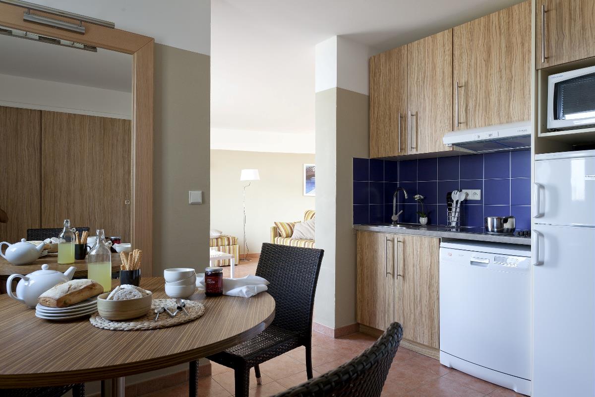 Et moderne kjøkken med treskap, et spisebord dekket til frokost og utsikt til en lys stue.