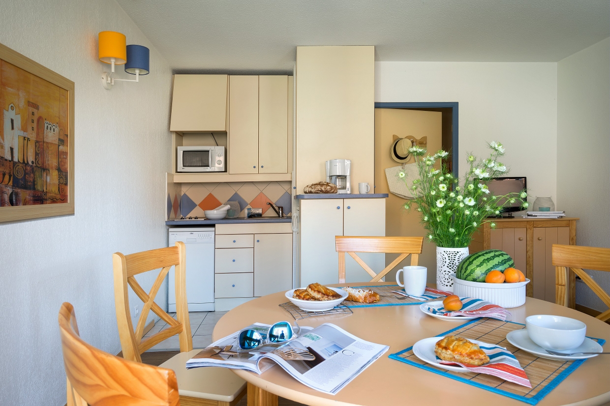Et koselig kjøkken og spiseplass med bakverk, frukt og blomster på et rundt frokostbord.