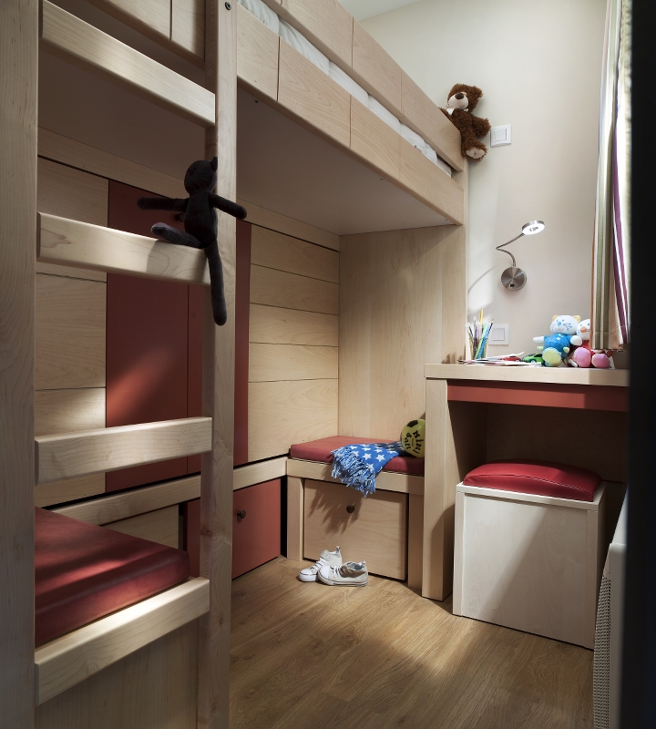 Lite, moderne barnerom med hems, skrivebord, leker og tregulv. På sengen og skrivebordet sitter det plysjbjørner.
