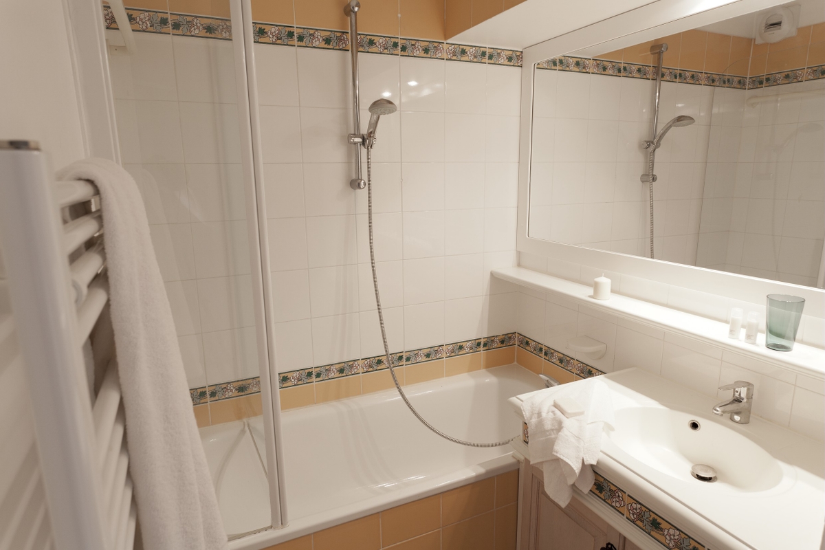 Moderne bad med badekar, dusj, vask, speil, hvite fliser og et håndkle som henger på en radiator.