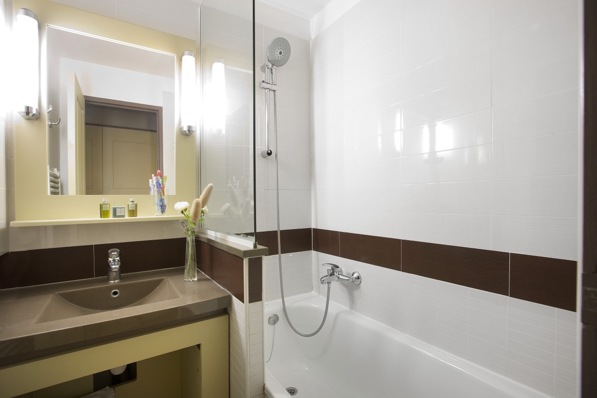 Moderne bad med brun benkeplate, vask, veggspeil, badekar og dusjvegg i glass.
