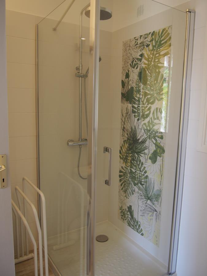 Dusj i glass med bladgrønt, botanisk design på den ene veggen og dusjhode i krom, sett fra inngangspartiet.