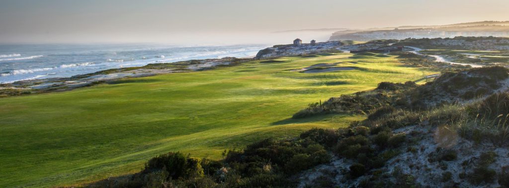 En naturskjønn kystgolfbane ved solnedgang, med frodige grønne fairways, sanddyner og bølger som ruller forsiktig mot kysten.