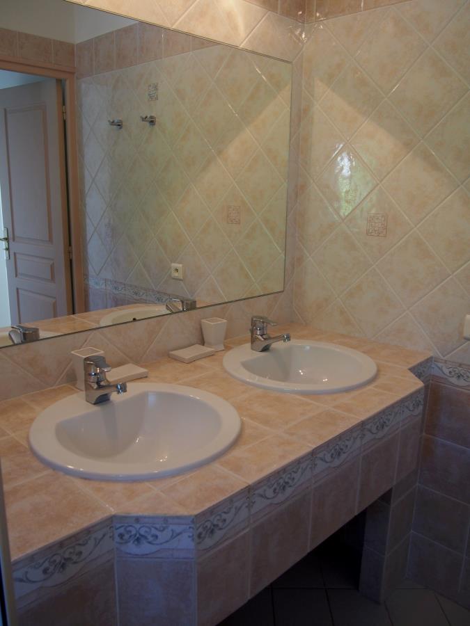 Badet er flislagt i beige med et stort speil og to hvite håndvasker med hver sin kran og en såpeskål i mellom.