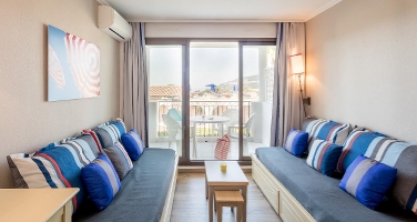 Lys stue med to blå sofaer, et lite bord og glassdører ut til en balkong med uteservering.