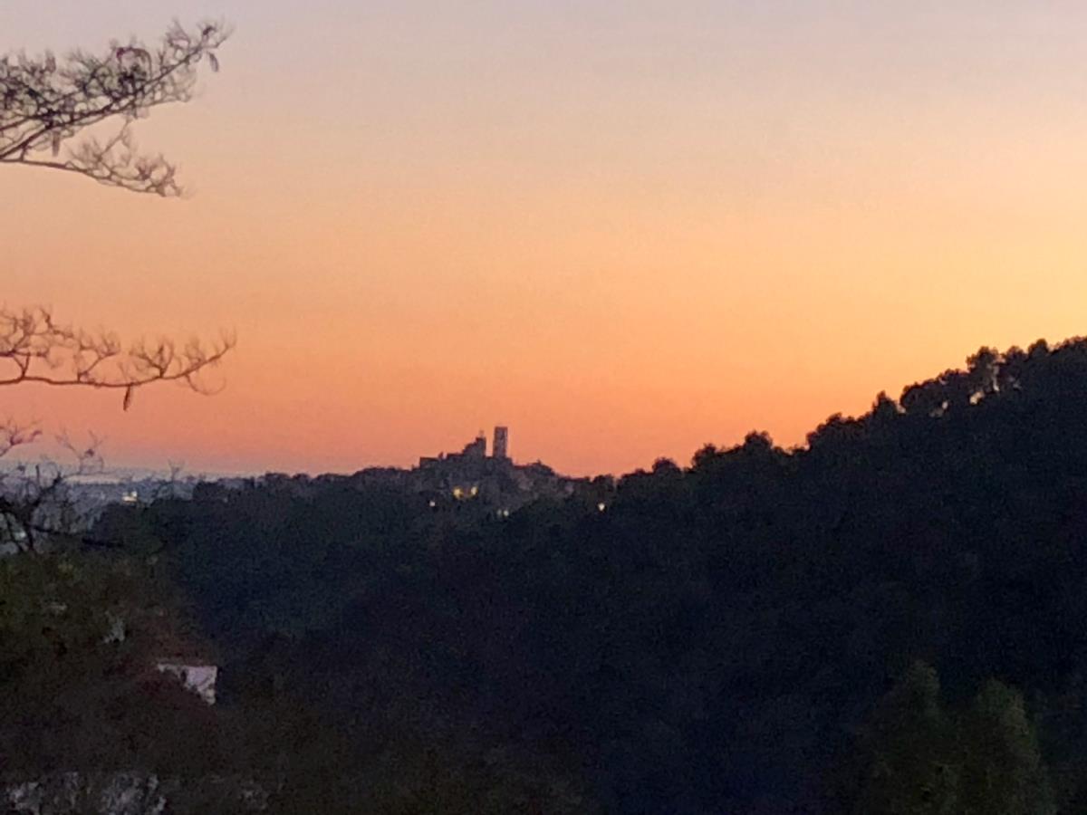 En silhuett av en by på en bakketopp i solnedgang, med en fargerik oransje og rosa himmel i bakgrunnen.